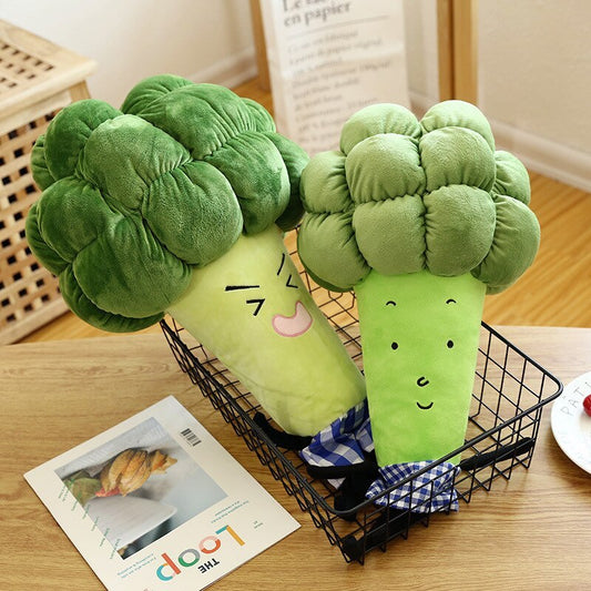 Two green plush broccoli toys in a black wire basket on a wooden table.