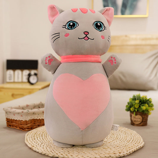 Gray cat-shaped plush toy with a pink heart on a bed in a bedroom setting