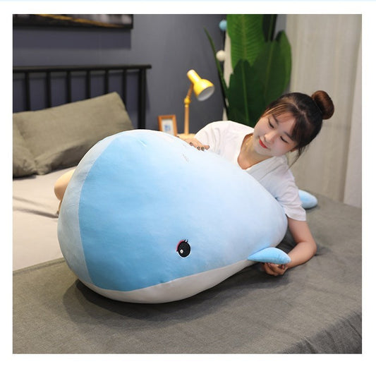 Person lying on a bed with a large blue whale-shaped pillow