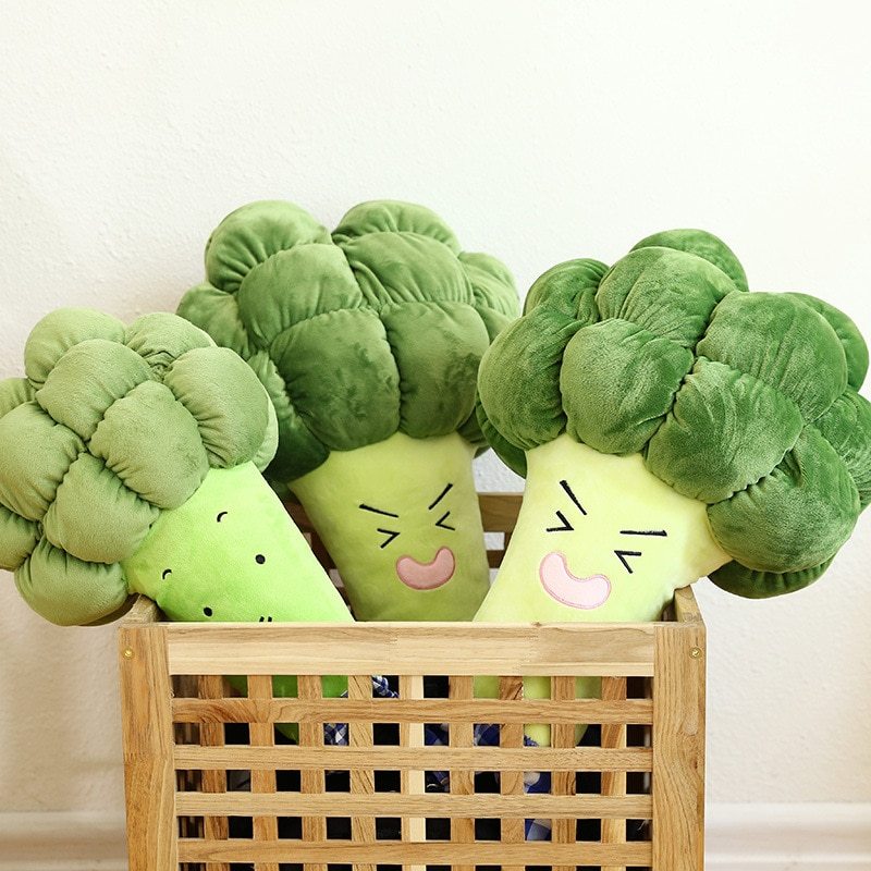 Plush broccoli toys with smiling faces in a wooden basket on a light background