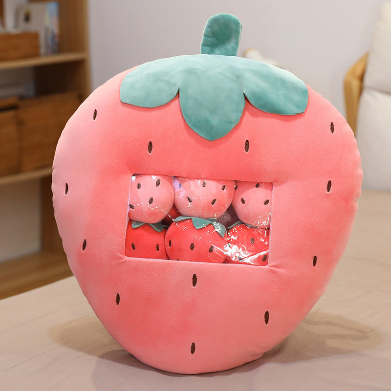 Plush strawberry-shaped pillow with small plush strawberries inside on a wooden surface.