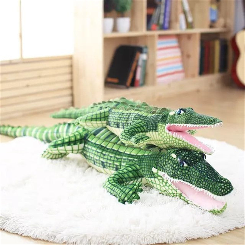 Two green crocodile plush toys on a white rug with a wooden shelf in the background.