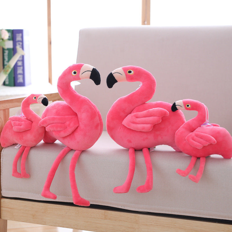 Four pink flamingo plush toys on a light-colored sofa.