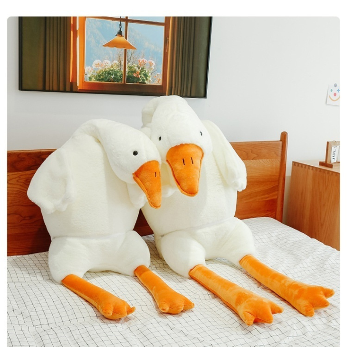 Two large white goose plush toys with orange beaks and feet on a bed.