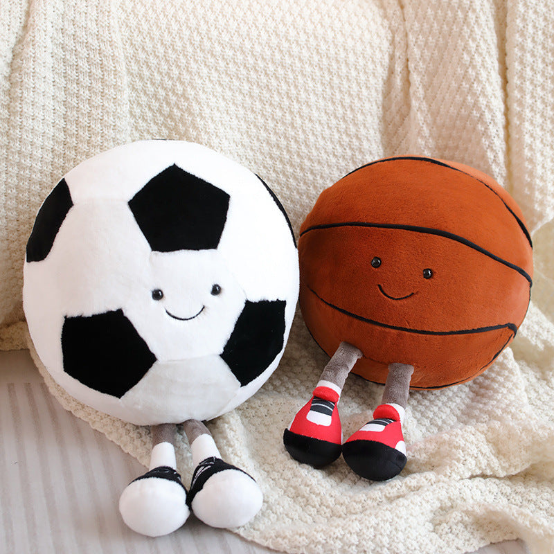 Plush toys shaped like a soccer ball and a basketball with smiling faces on a soft surface.